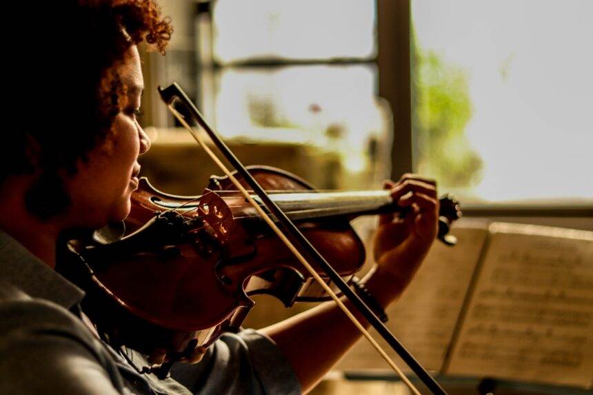 A woman playing violin with the musical notes in front of her. There is a musical fete of Candlelight featuring Bach and the Beatles.