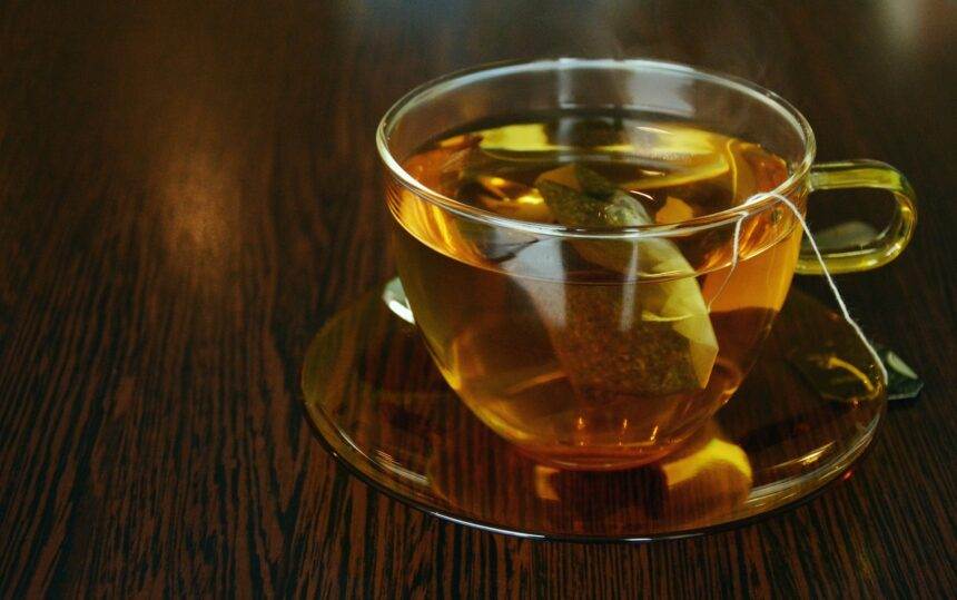 A picture of a cup of tea in a glass cup and saucer on the brown wooden table. The idea of beating plastic pollution this International Tea Day.