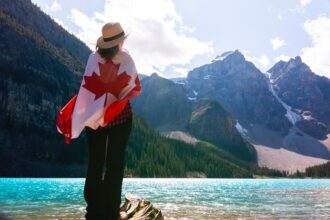 A woman wrapped around a Canadian flag and standing near a water body.