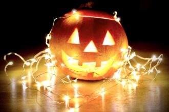 A carved pumpkin decorated with lights on the floor.
