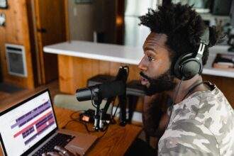 A person, with a mic on and an open laptop, recording a podcast.
