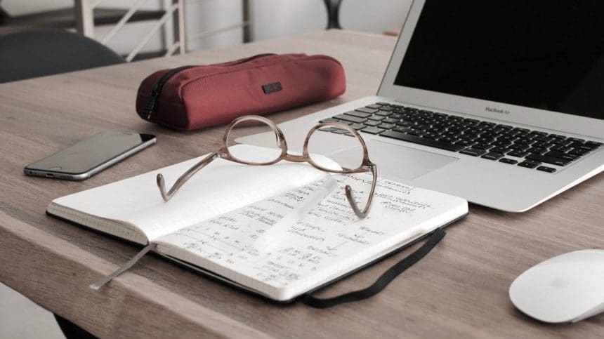 A spectacle kept on an open book in front of a laptop.