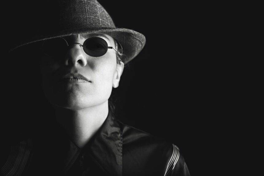 A black and white photo of a man wearing black goggles and a Fedora hat.