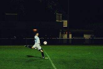 A person kicks a soccer ball in the field during the night.