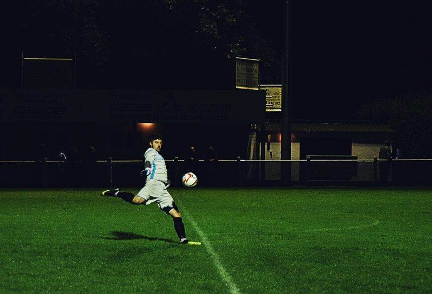 A person kicks a soccer ball in the field during the night.