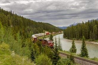 A train coming on the railway line in the Banff National Park with mountains in the background.
