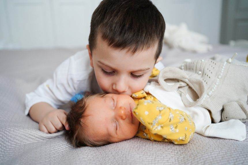 An older brother kissing the head of the infant brother.