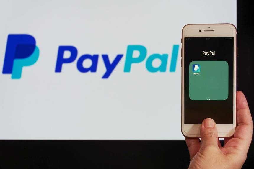 Person holding smartphone with PayPal app on screen, online payment service concept.