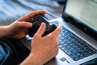 Person playing video games using a controller and laptop setup.