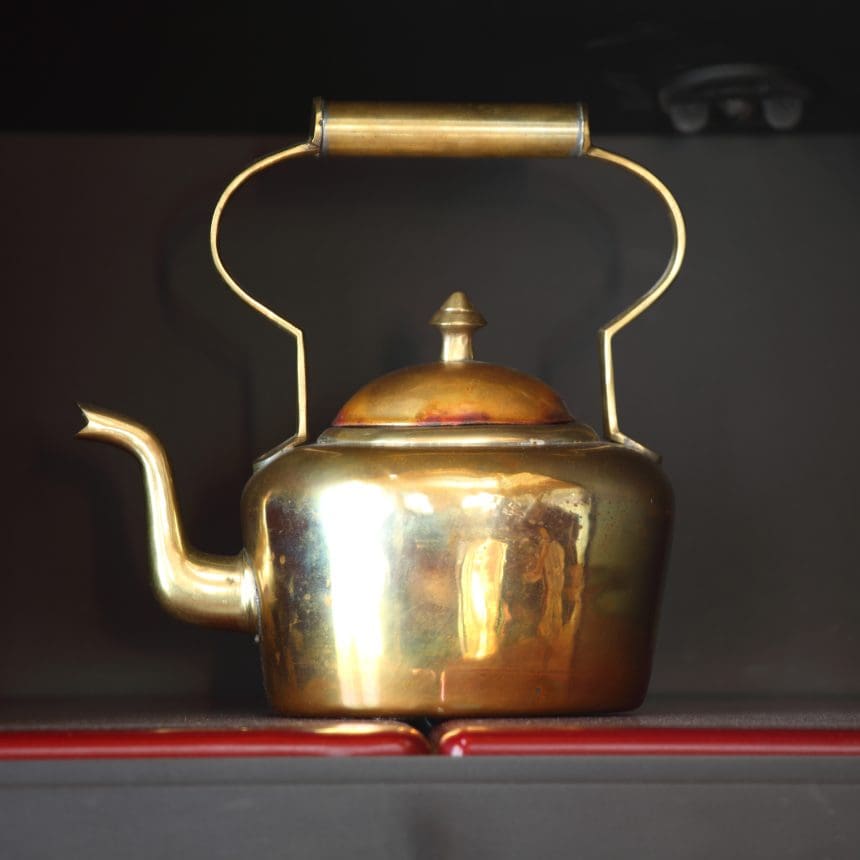Antique brass teapot on dark shelf.