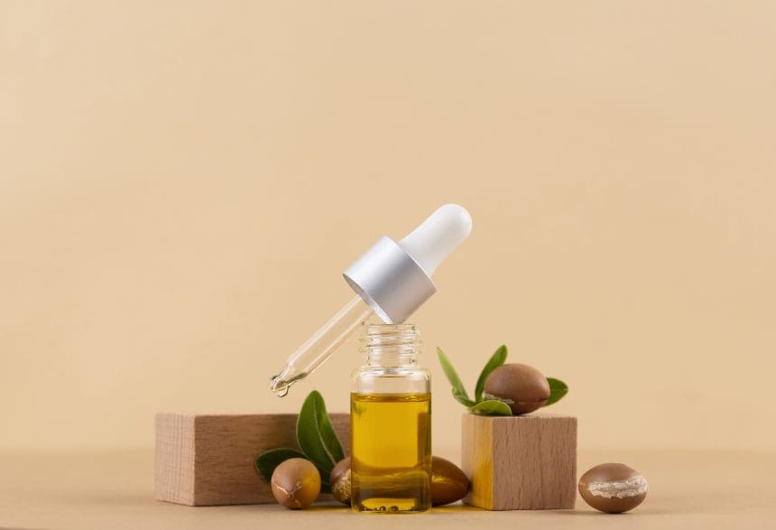 Bottle of castor oil with dropper and beans on wooden block.