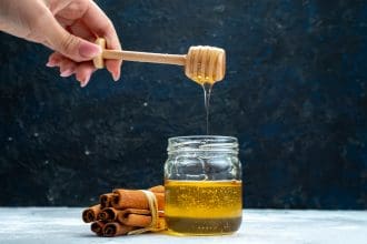 Drizzling honey from dipper into jar with cinnamon sticks.