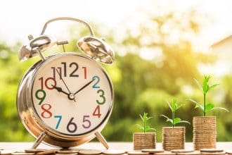 Alarm clock with growing money stacks representing time investment concept.