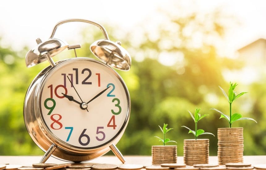 Alarm clock with growing money stacks representing time investment concept.